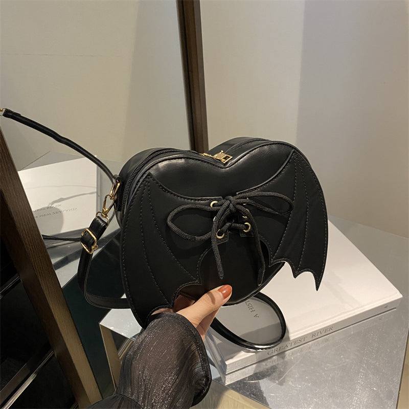 Bat-Wing Heart Crossbody Bag, black, held in hand